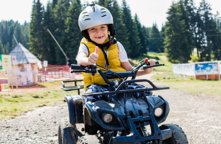 Happy kid on quadbike showing thumbs up while looking at camera.